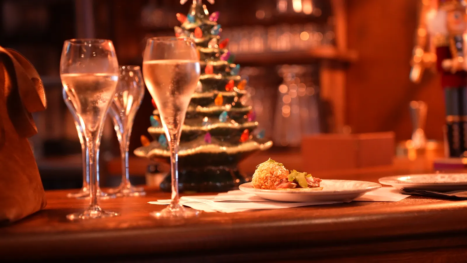 Two flutes of prosecco on the bar in front of a lit ceramic Christmas tree
